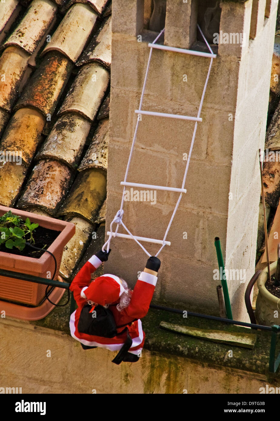Father Christmas trying to climb a chimney with the aid of a stepladder so he can get inside the house and deliver presents! Stock Photo
