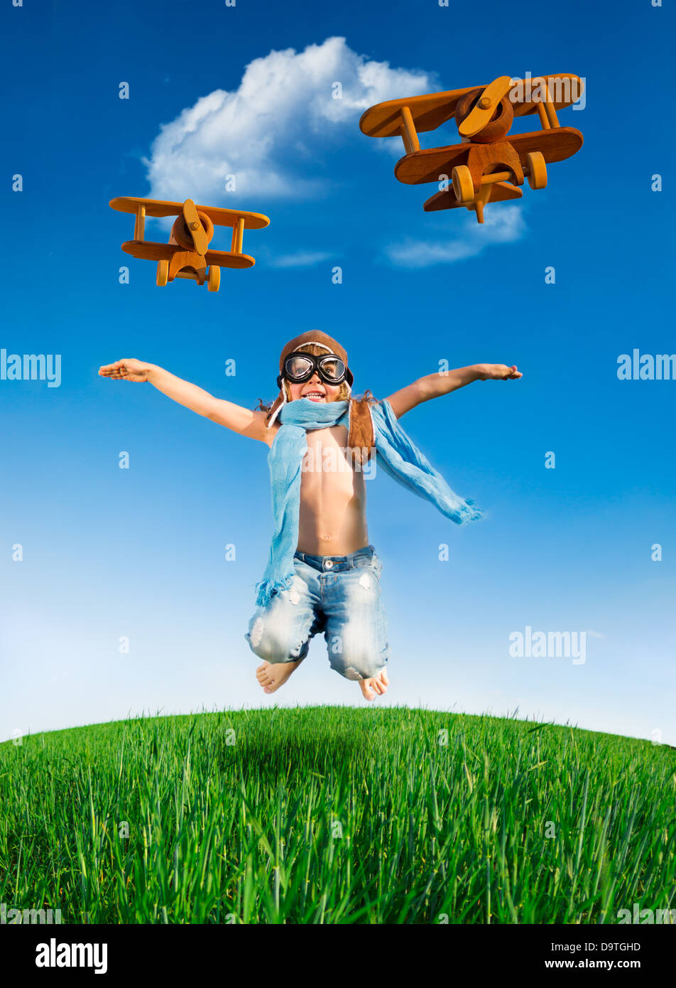Happy kid dressed as a pilot jumping in green field against blue sky. Summer vacation concept Stock Photo