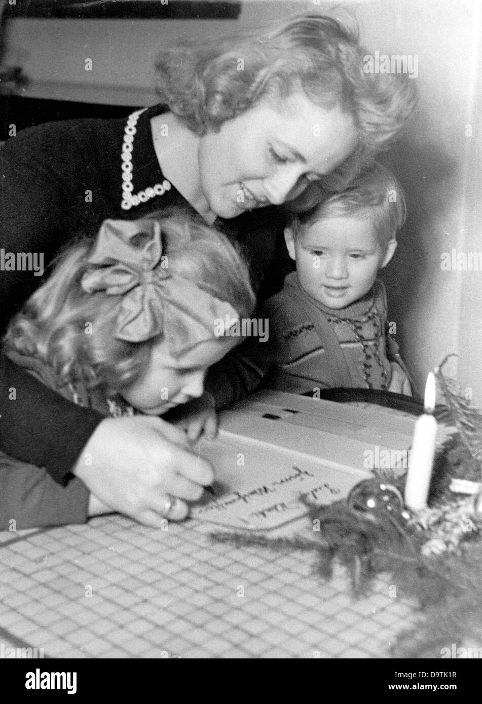 A woman is writing a letter to husband and father, who has gone to war as a soldier of the German Wehrmacht. Location unknown. The National Socialist propaganda text on 13 December 1944 on the back of the picture: 'We are writing a Christmas letter to daddy afield.' Fotoarchiv für Zeitgeschichte Stock Photo