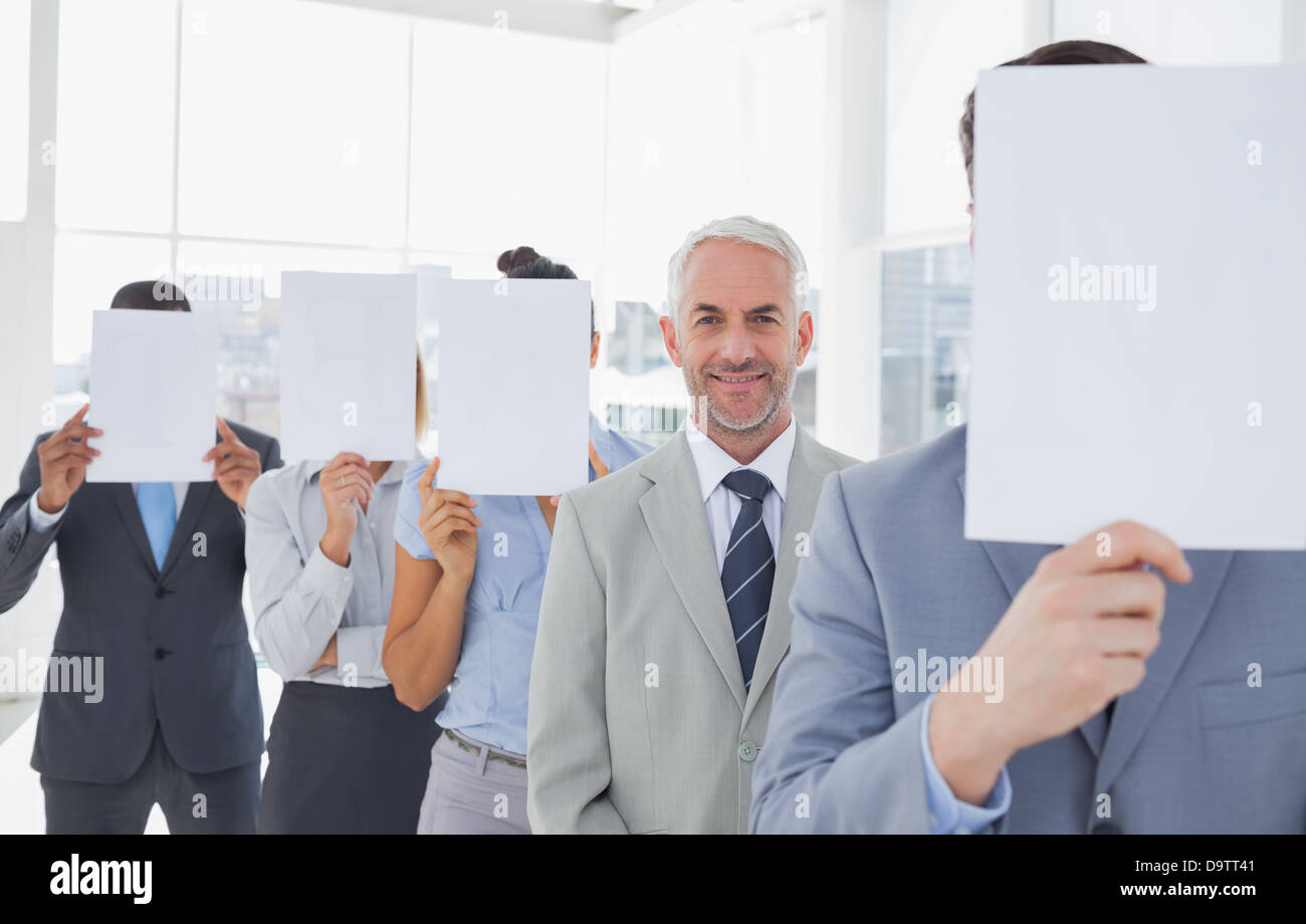 Business team covering face with white paper except for one Stock Photo