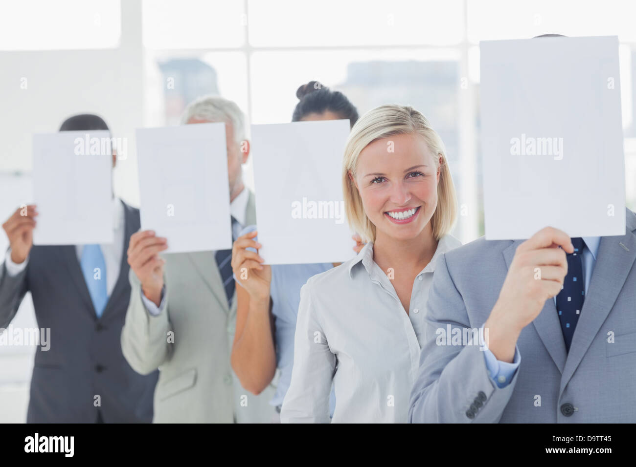 Business team covering face with white paper except for one woman Stock Photo
