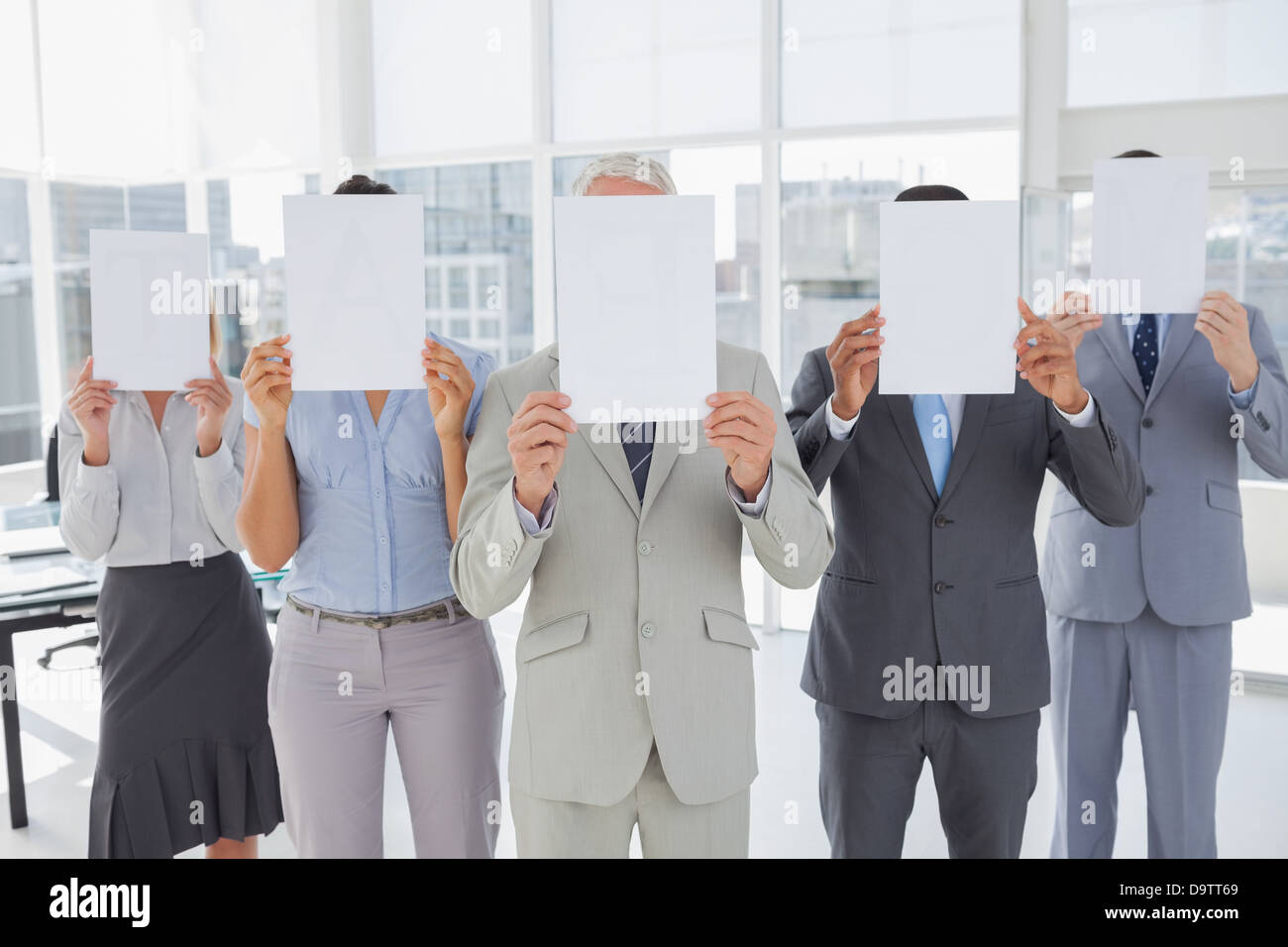 Buisness team holding up blank pages and covering their faces Stock Photo