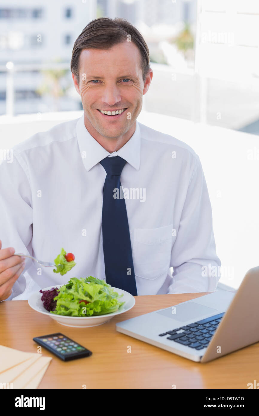 Cheerful businessman eating a salad on his desk Stock Photo