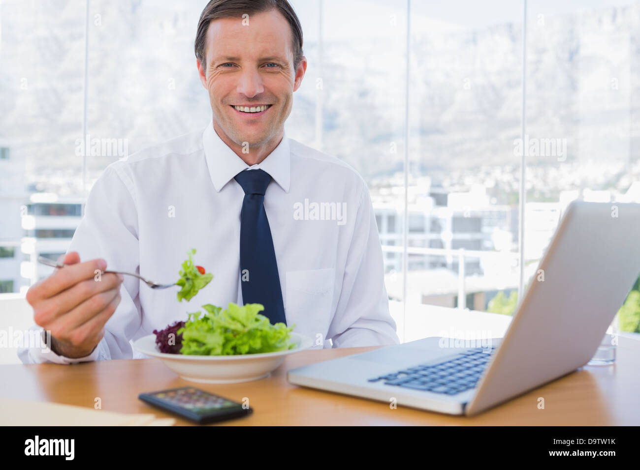 Happy businessman eating a salad on his desk Stock Photo