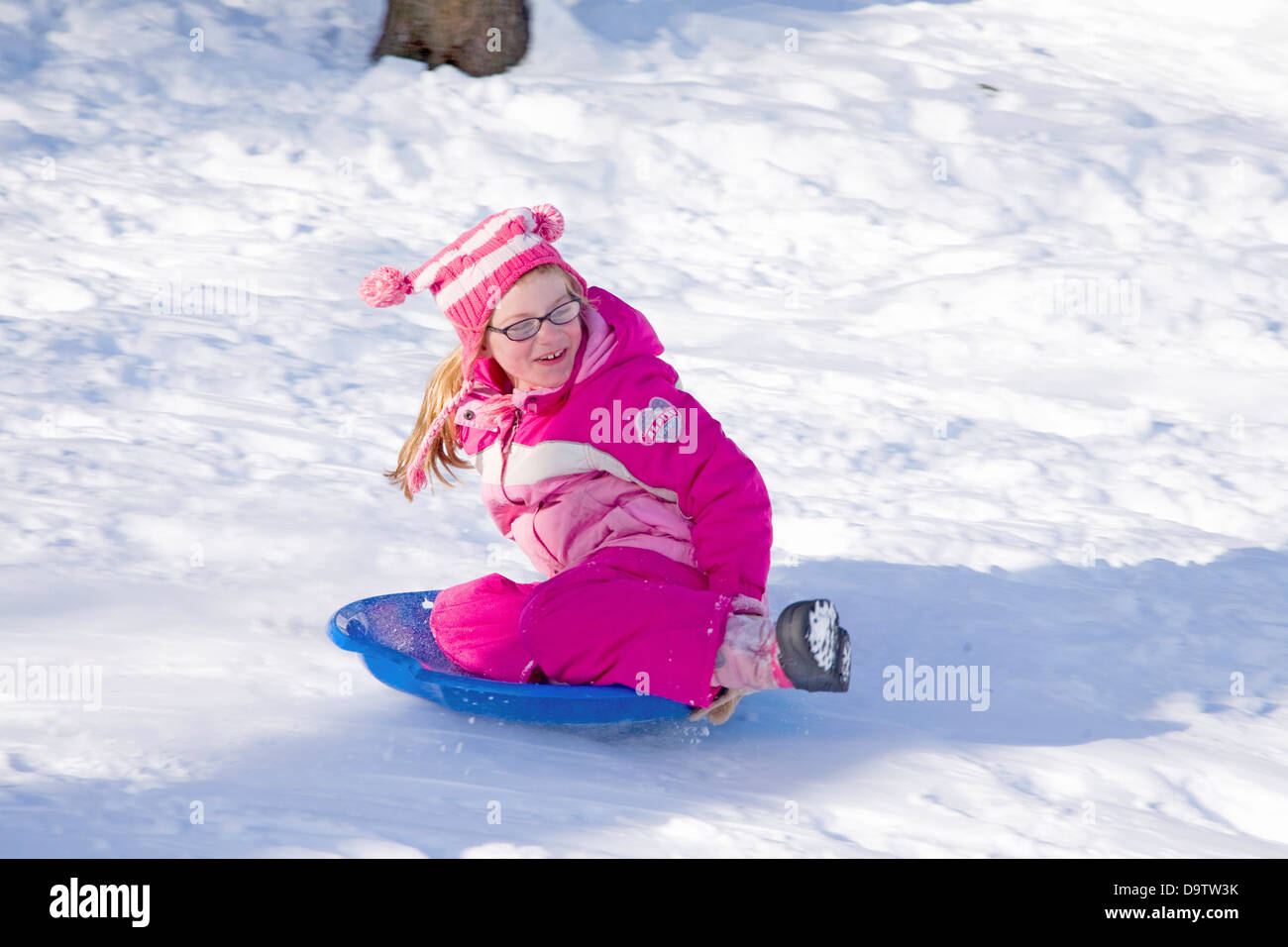 Little girl in pink snowsuit slides down hill in fresh snow near Lexington, Ma., New England