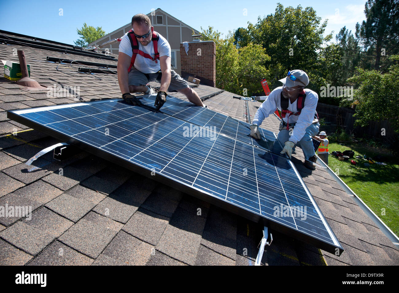 Construction workers install a Photovoltaic Solar Electric System on the roof of a home September 10, 2012 in Englewood, Colorado. Stock Photo