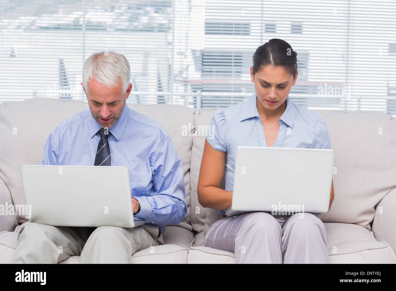 Business people sitting on sofa using their laptops Stock Photo Alamy