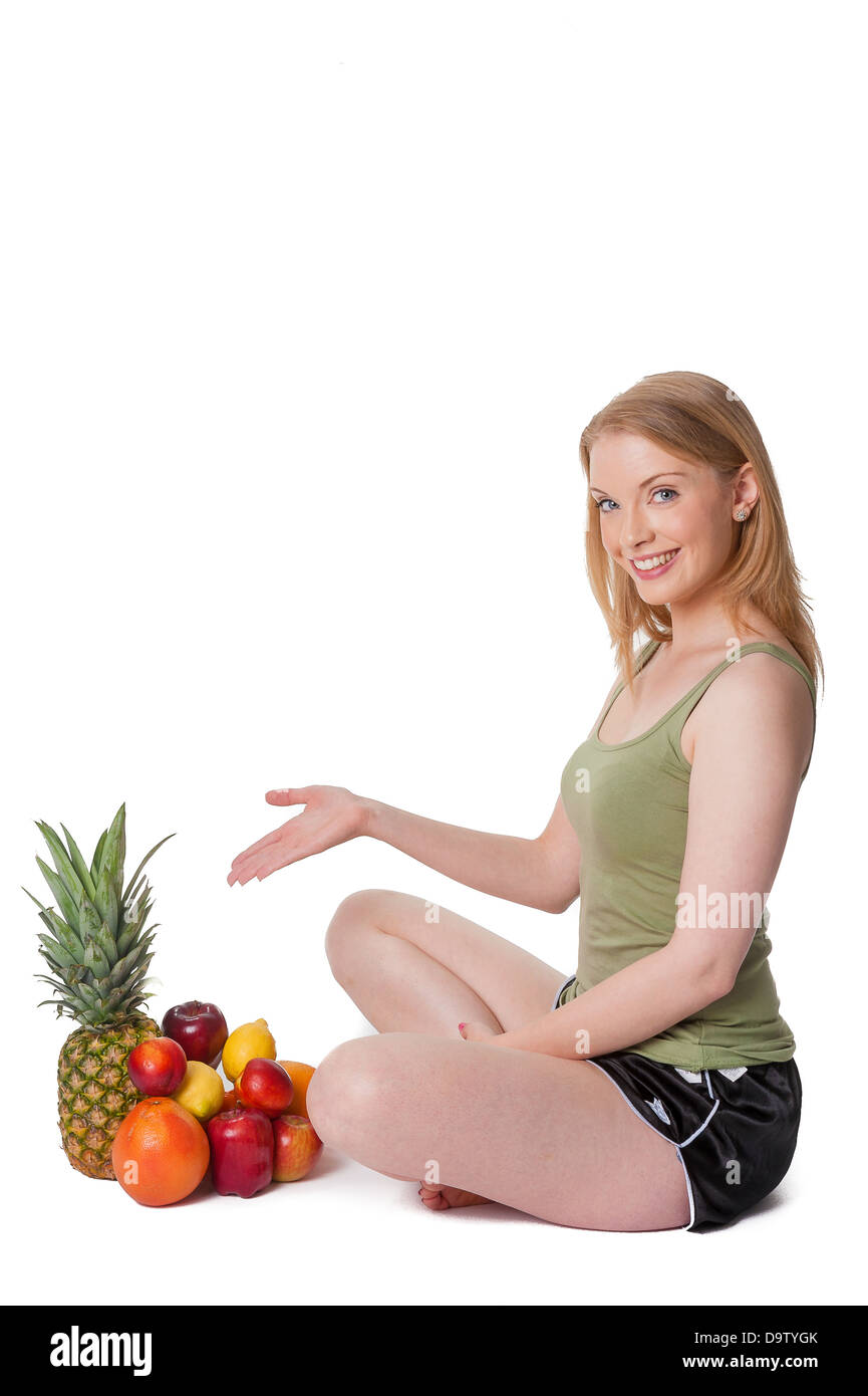 Happy young woman sitting crosslegged, showing fresh fruit selection