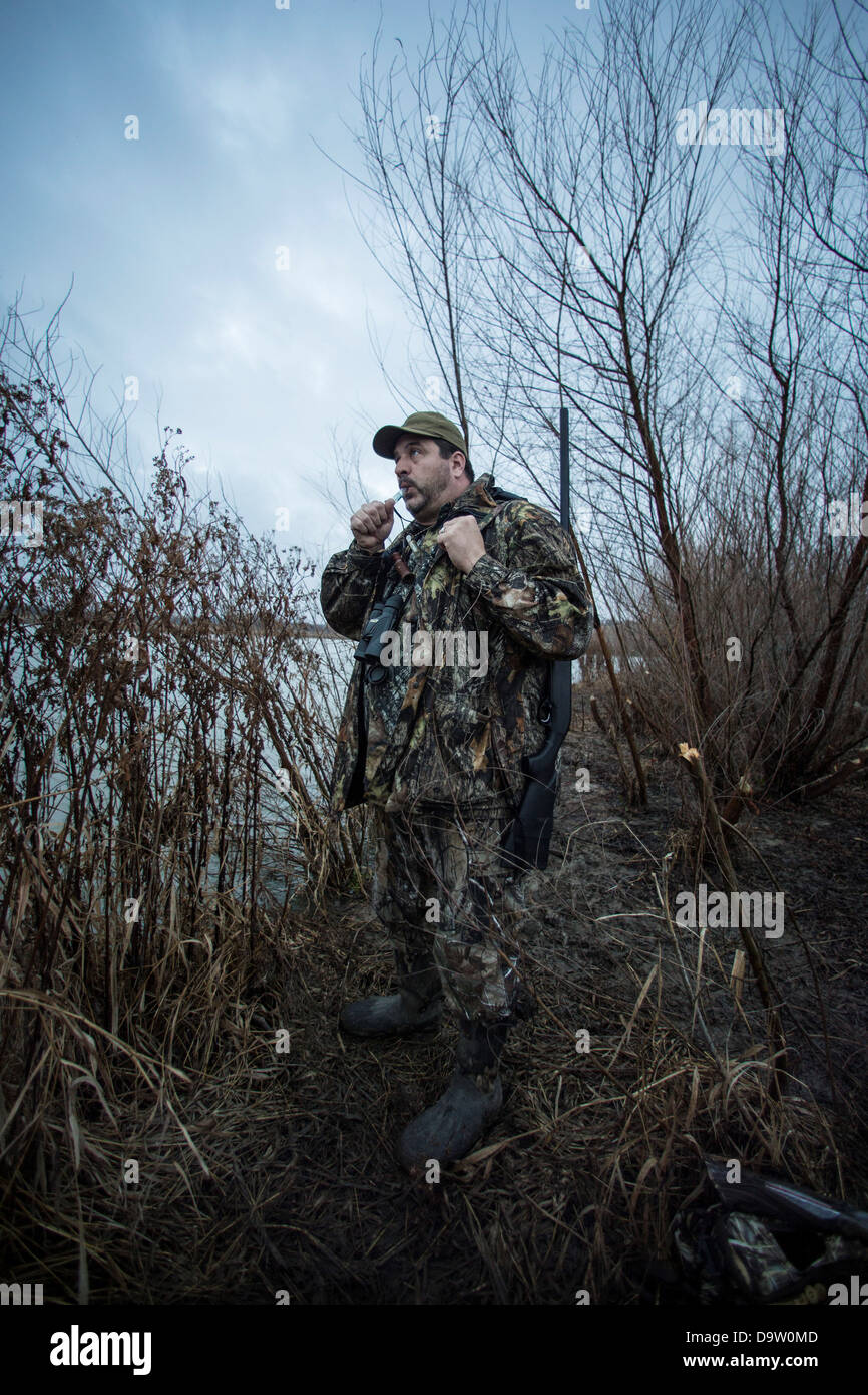 Hunter standing near lake using duck call Stock Photo Alamy