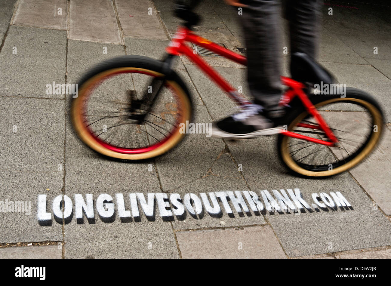 A BMX rider cycles past a stencil advertising the website url  longlivesouthbank.com Stock Photo - Alamy