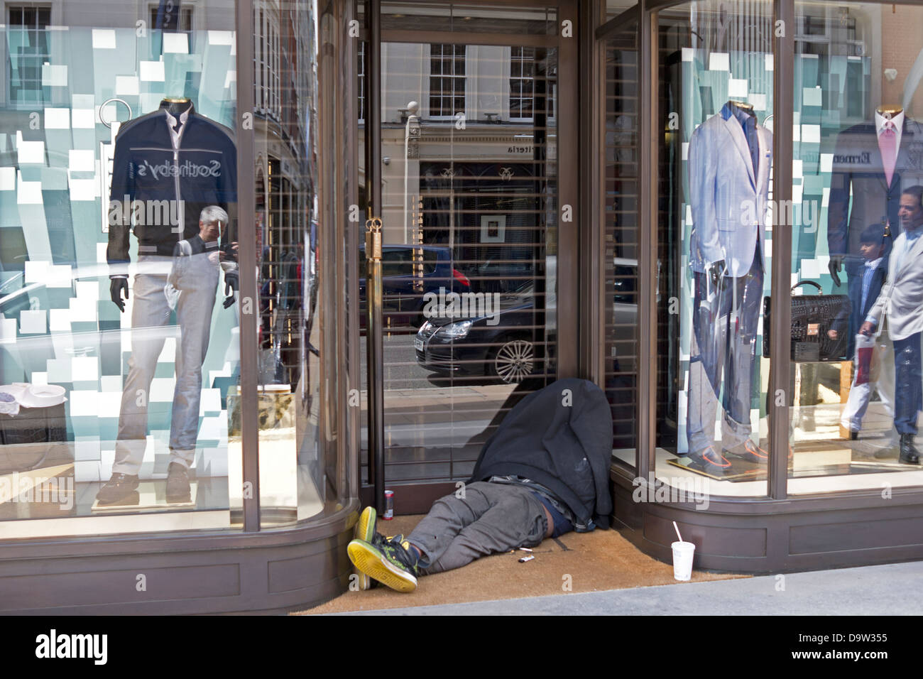A homeless person is slumped in a doorway of an upmarket clothes store. Landscape view. Stock Photo