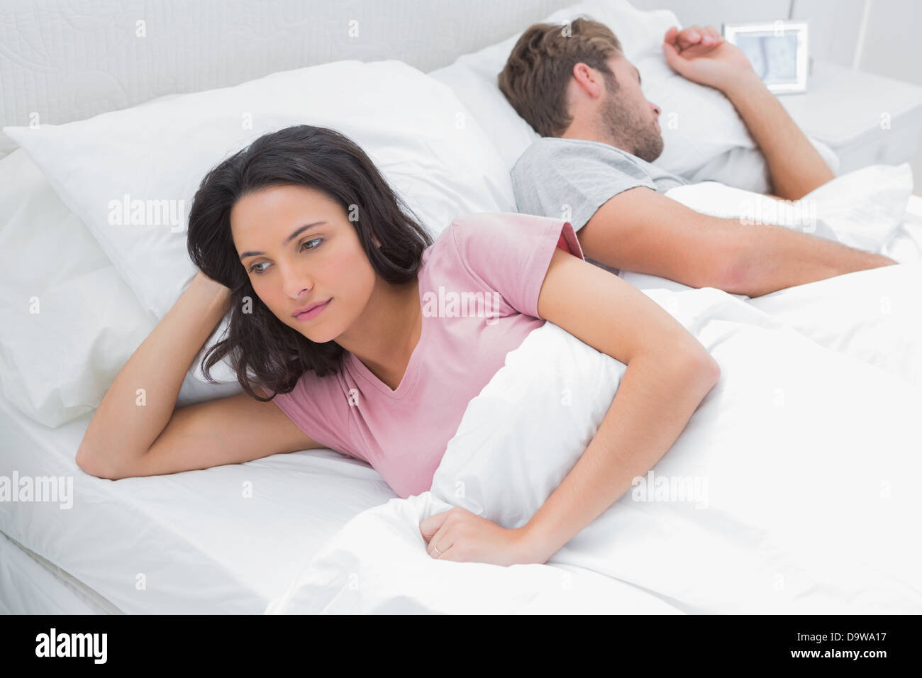 Woman thinking in her bed next to her sleeping husband Stock Photo