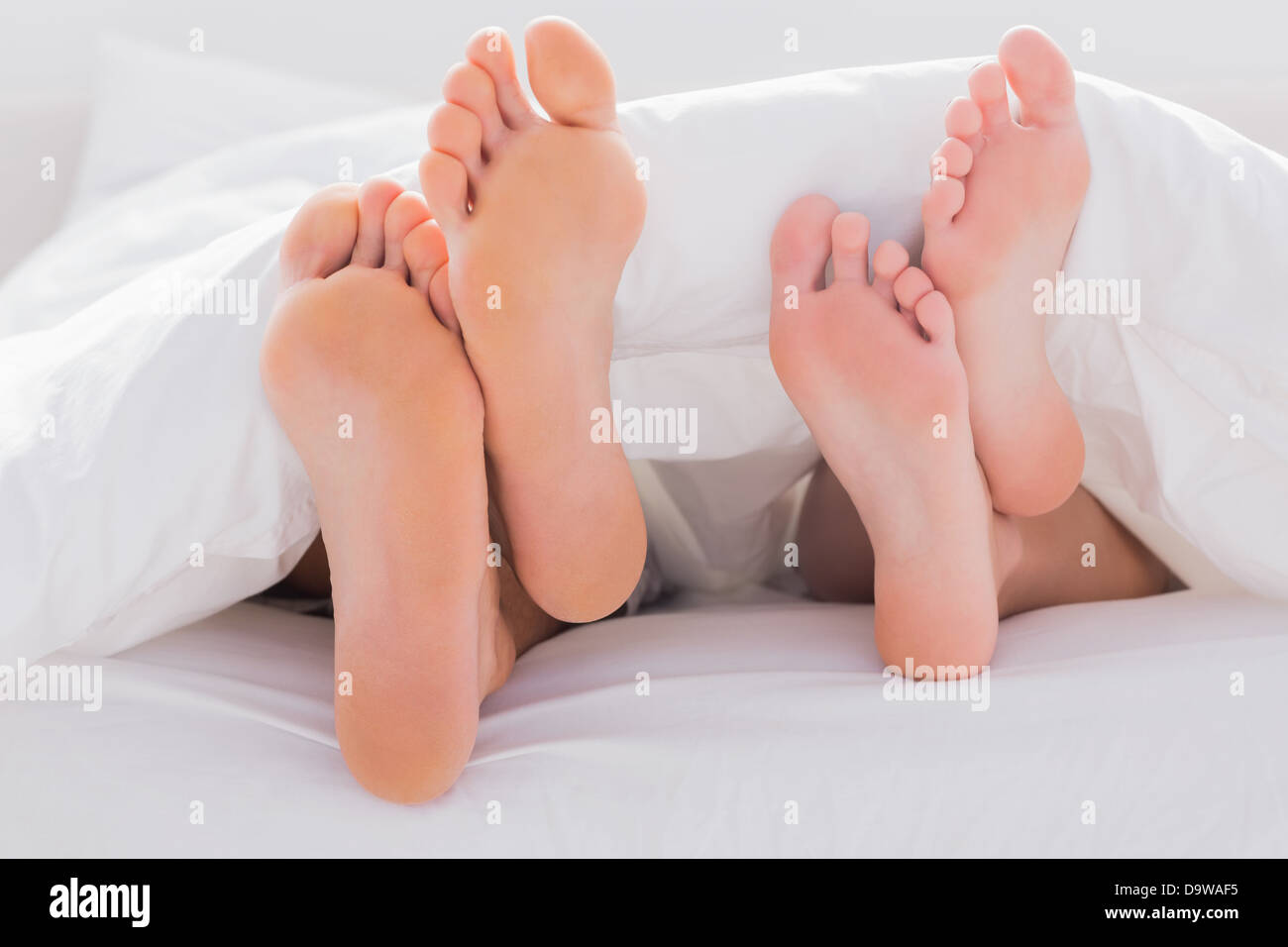 Couples feet crossed under the duvet Stock Photo