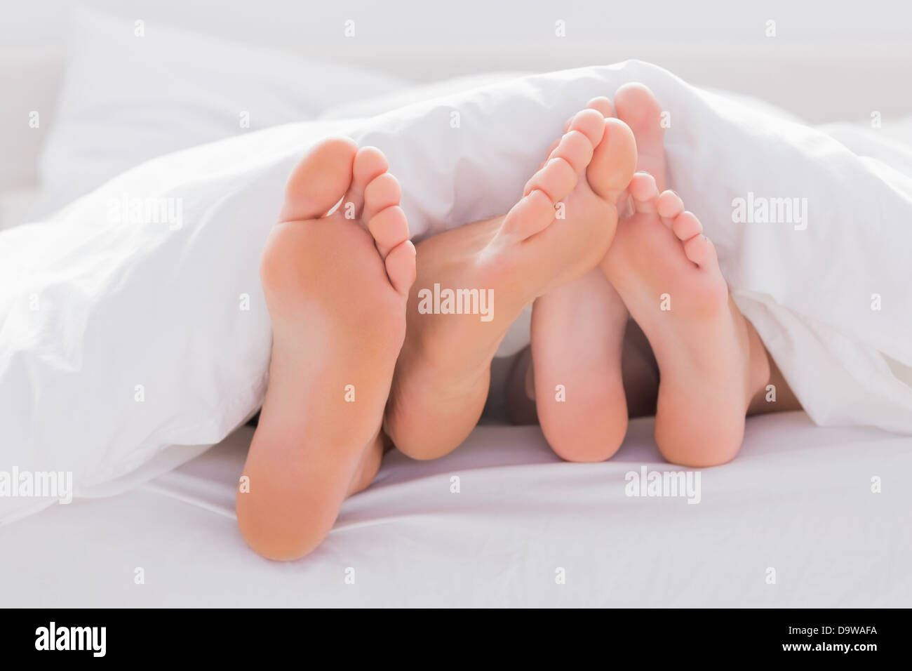 Couple rubbing their feet together under the duvet Stock Photo