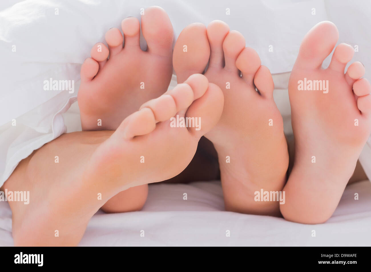 Couple touching their feet together under the duvet Stock Photo