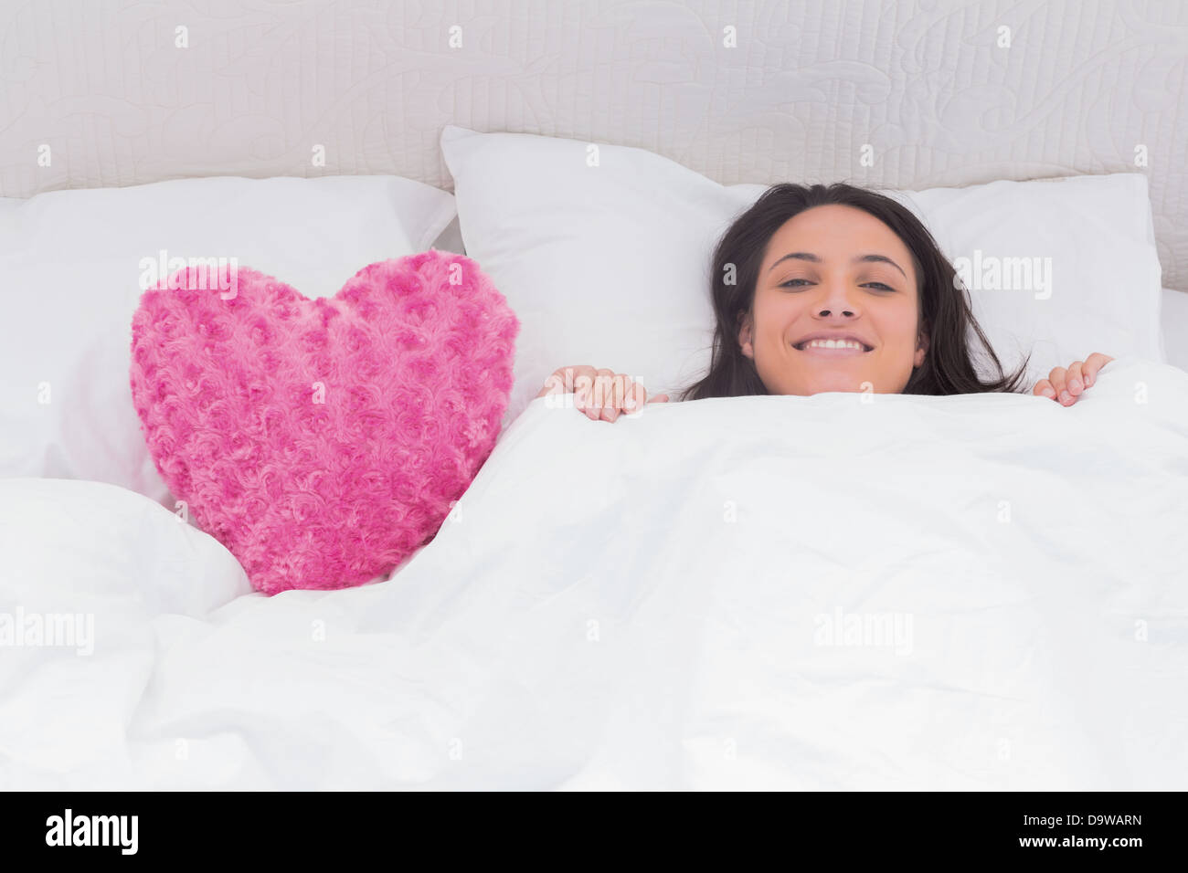 Woman lying in bed next to a fluffy heart pillow Stock Photo