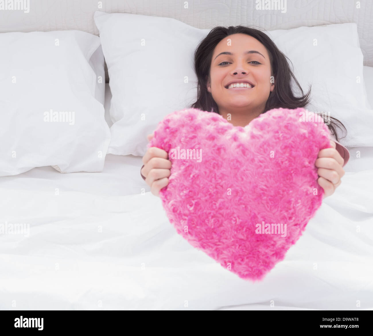 Woman in her bed holding a fluffy heart cushion Stock Photo Alamy