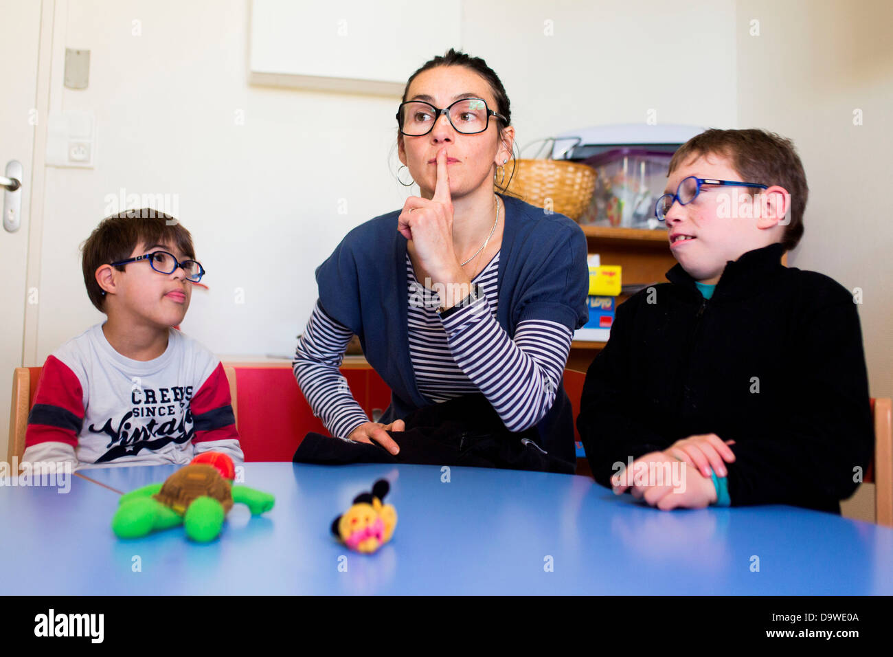 7 years old boys down's syndrome educated in an IME Special education teacher teaching sign language Medical-Educational Stock Photo