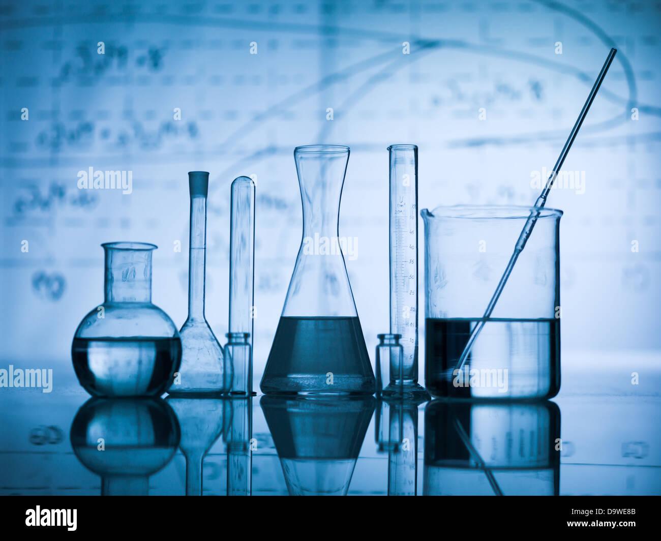 Group of laboratory flasks empty or filled with a clear liquid on blue tint scientific graphics background and their reflection Stock Photo