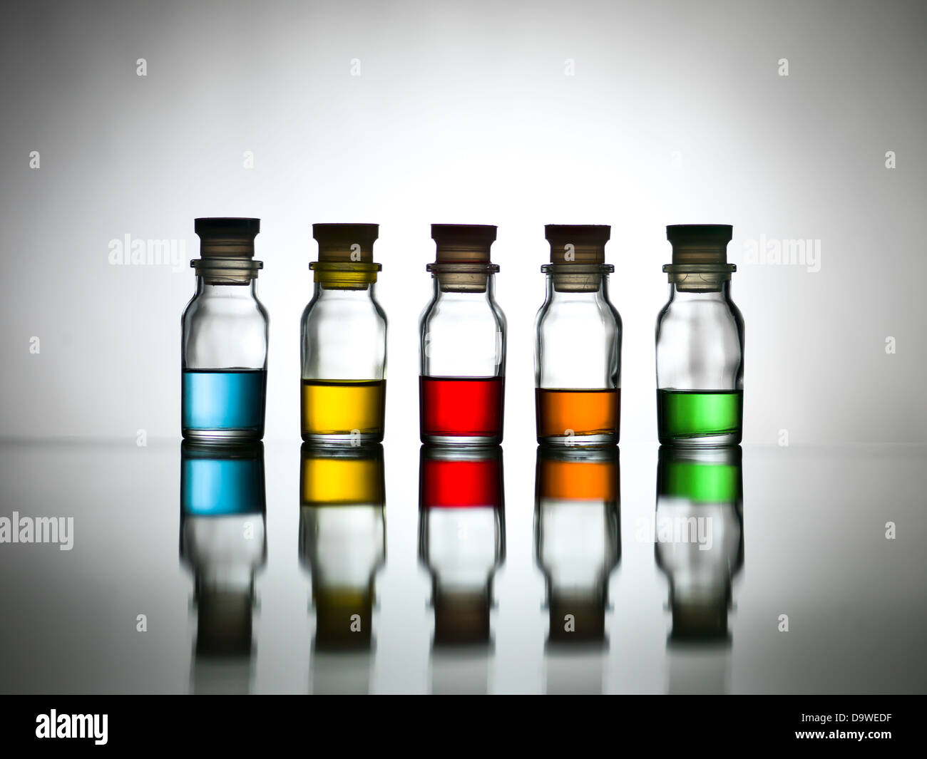 Five bottles with diverse colors of content reflected on a table Stock Photo