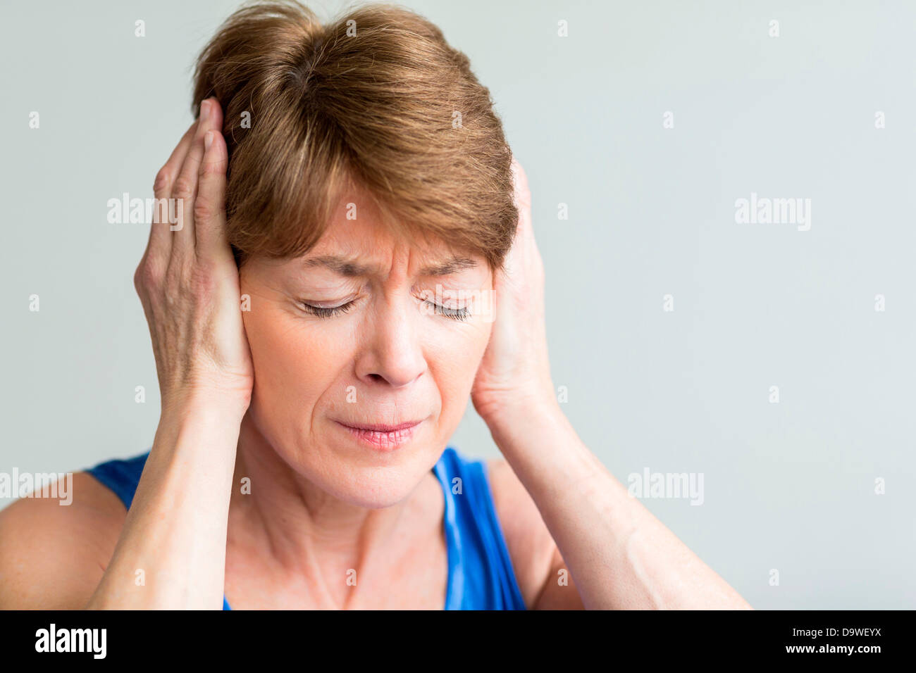 Senior woman holds her hands to her painful ears Stock Photo