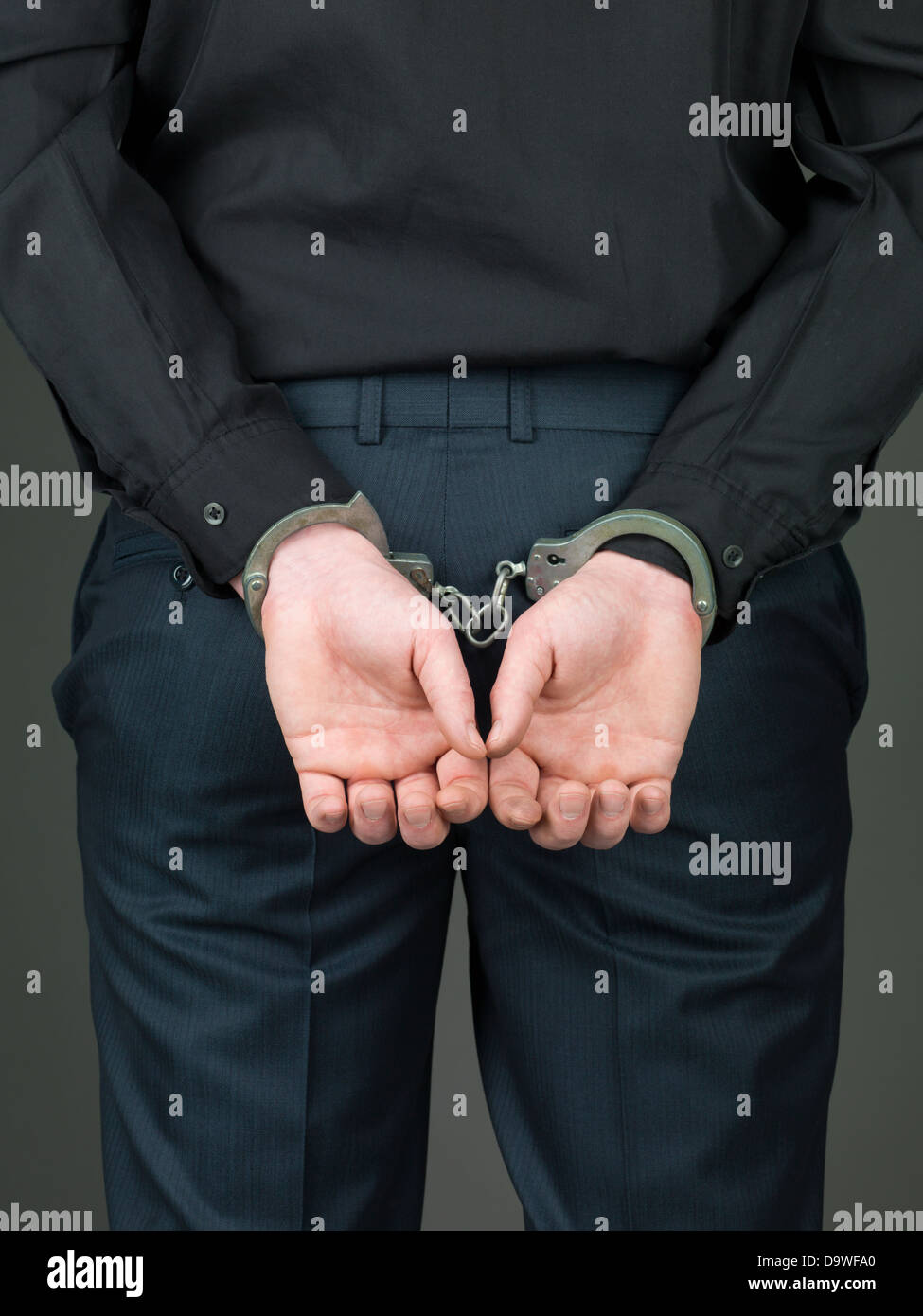 back view of a person dressed in black; handcuffed with their hands behind their back and their palms open Stock Photo