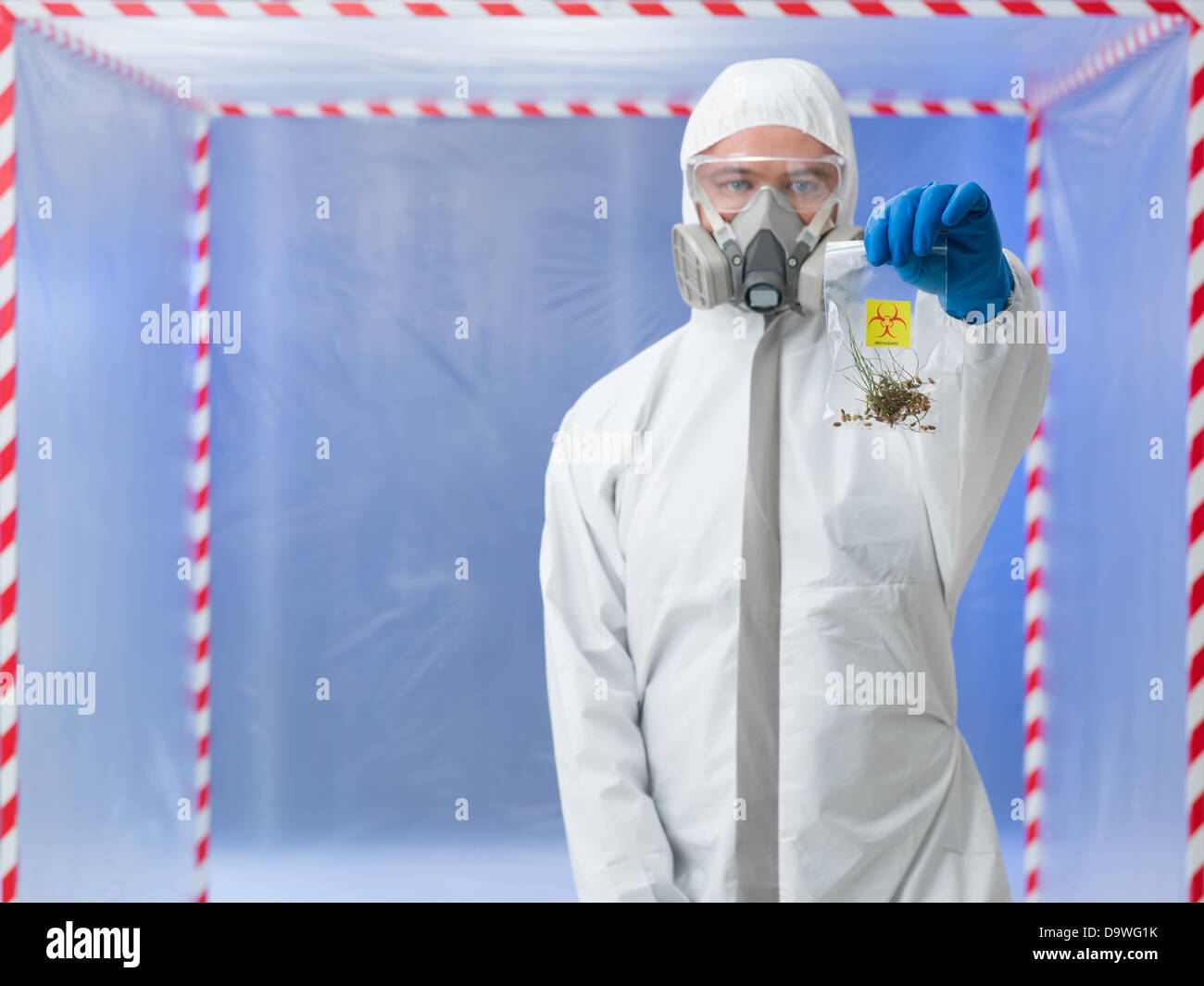 close-up of man wearind protection equipment, holding a plastic bag with germinated seeds, in a chamber surounded with red and white tape Stock Photo