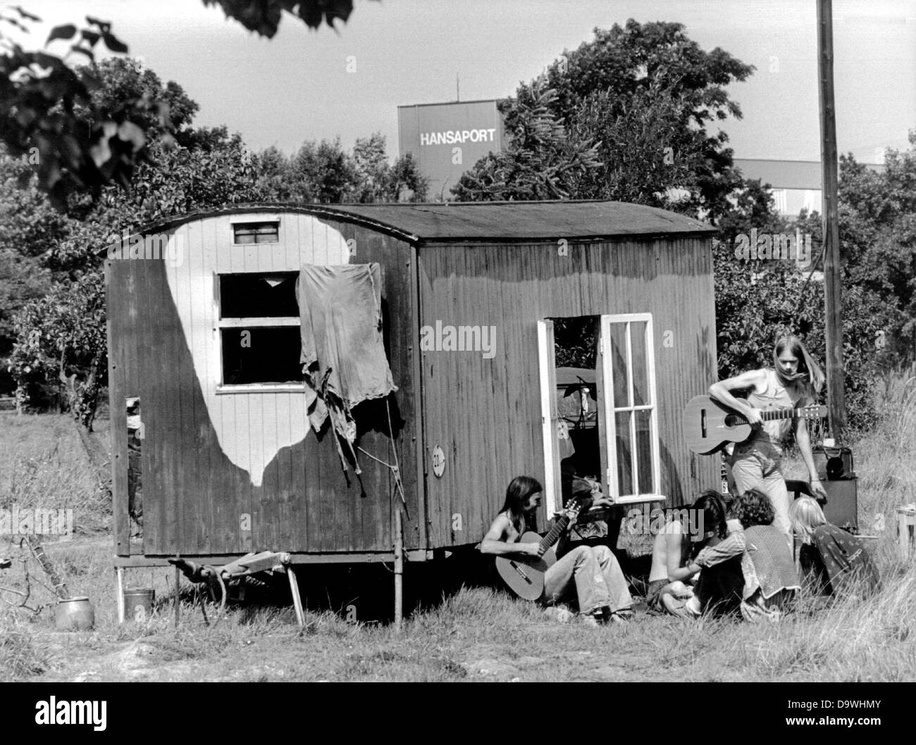 A group of young people talks and plays guitar in front of a construction trailer in Hamburg-Altenwerder on the 25th of August in 1979. Numerous houses were torn down due to the harbour expansion, so that young people put up their tents and moved into construction trailers in protest. Stock Photo