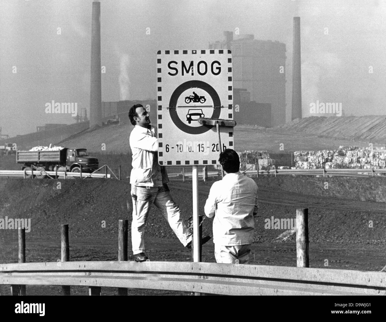 Two workers clean a smog sign in Dortmund in front of an industrial scenery on the 29th of October in 1975. In case that the acceptable values will be exceeded, drivers have to expect a driving ban. Stock Photo