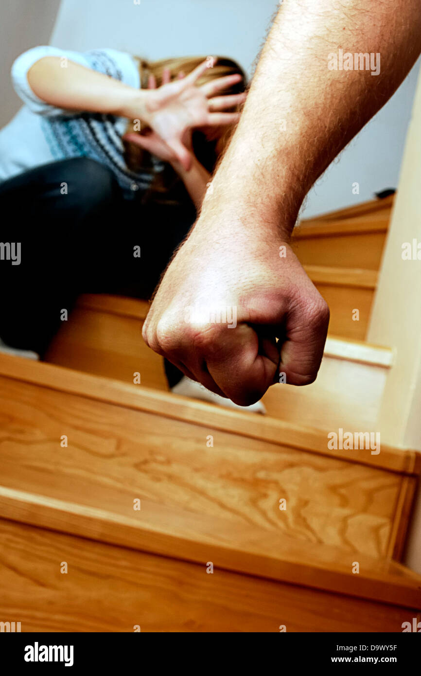 menacing male hand with an afraid woman crouched in the background - domestic violence concept Stock Photo