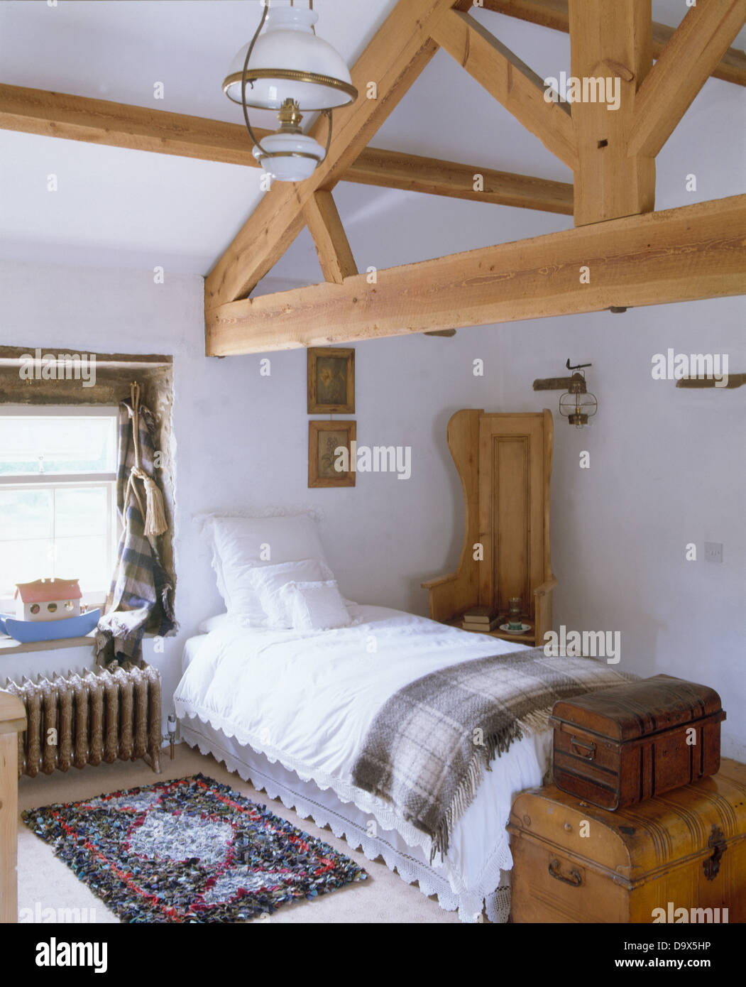 Wooden apex beams in country loft conversion bedroom with white bedlinen and plaid rug on single bed and rag rug on floor Stock Photo