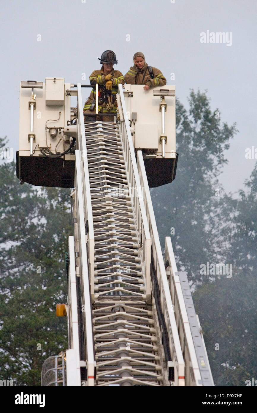 Two female fire fighters on top of a bucket ladder while fighting a house fire Stock Photo Alamy