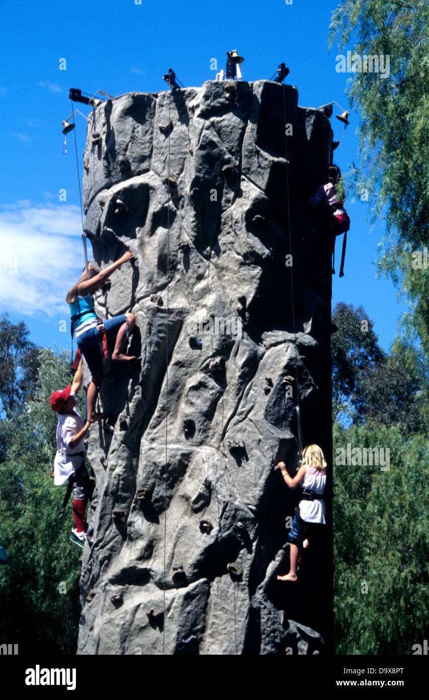 children climb up portable rock climbing wall at public park Stock
