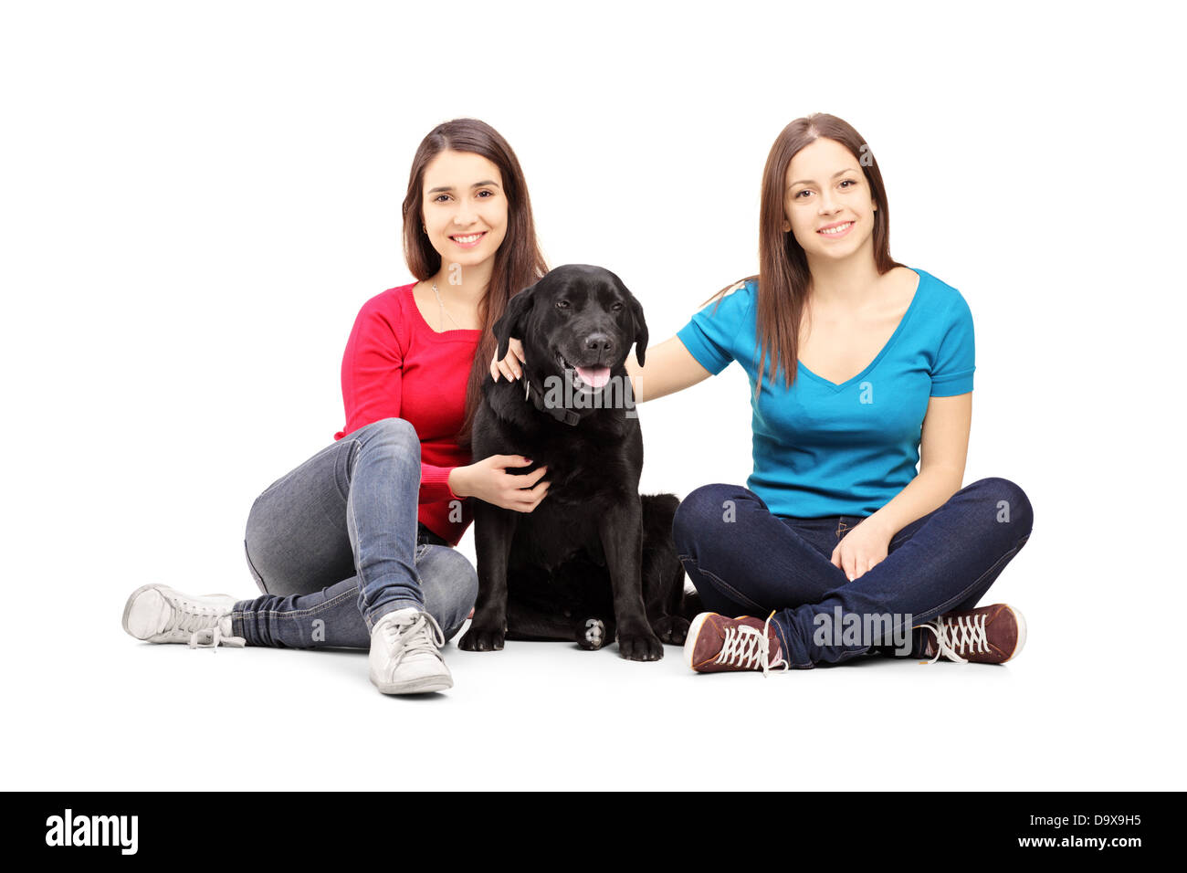 Two female friends sitting on a floor and posing with a black dog Stock Photo