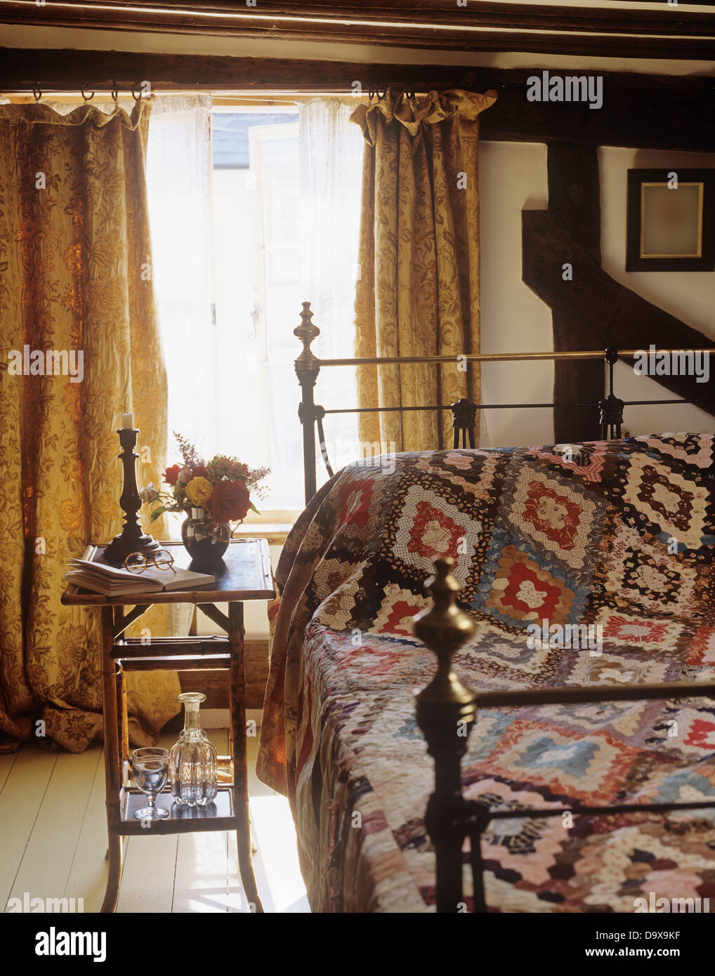 Small Bamboo Table Beside Brass Bed With Patchwork Quilt In