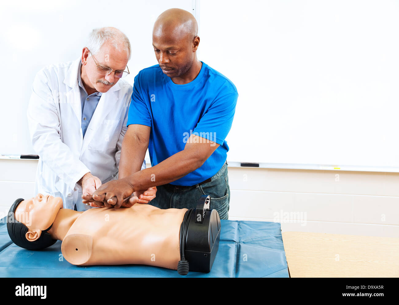 Doctor teaching first aid CPR techniques to an adult, African-american student. Room for text.  Stock Photo