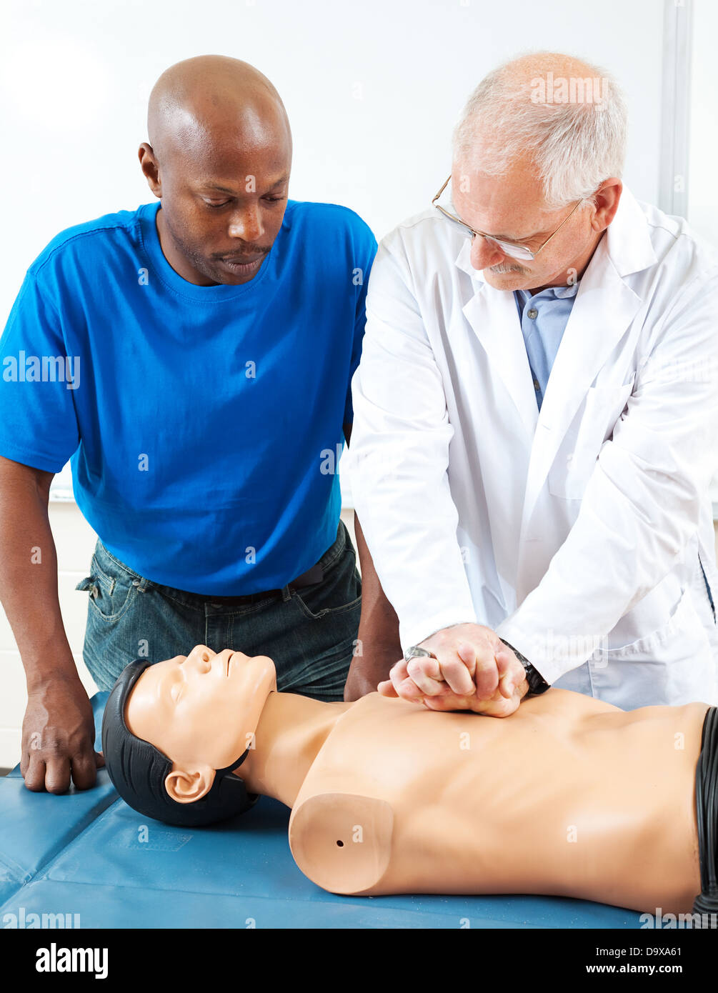 Mature doctor teaching an adult student how to perform CPR, using a dummy.  Stock Photo