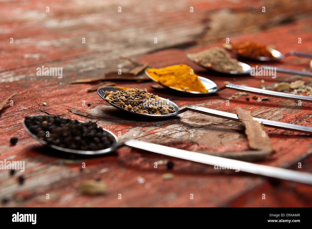 Table spoons heaped with different spices on an orange textured wooden surface. Artistic use of shallow depth of field. Stock Photo