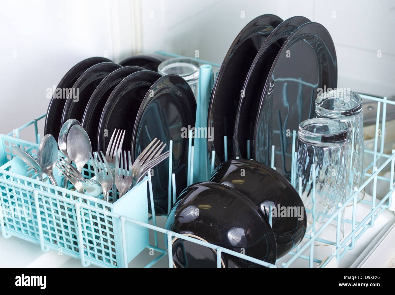 Dishwasher rack loaded with clean plates, glasses and silverware. Stock Photo