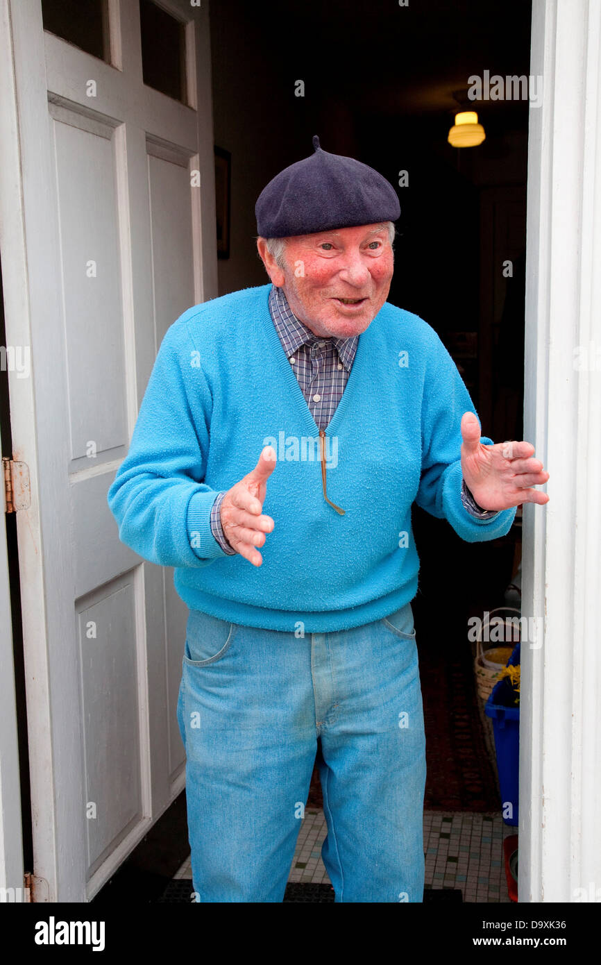 Senior Italian-American man in blue seater matching hat gestures smiles in front his home in historic North End Italian section Stock Photo