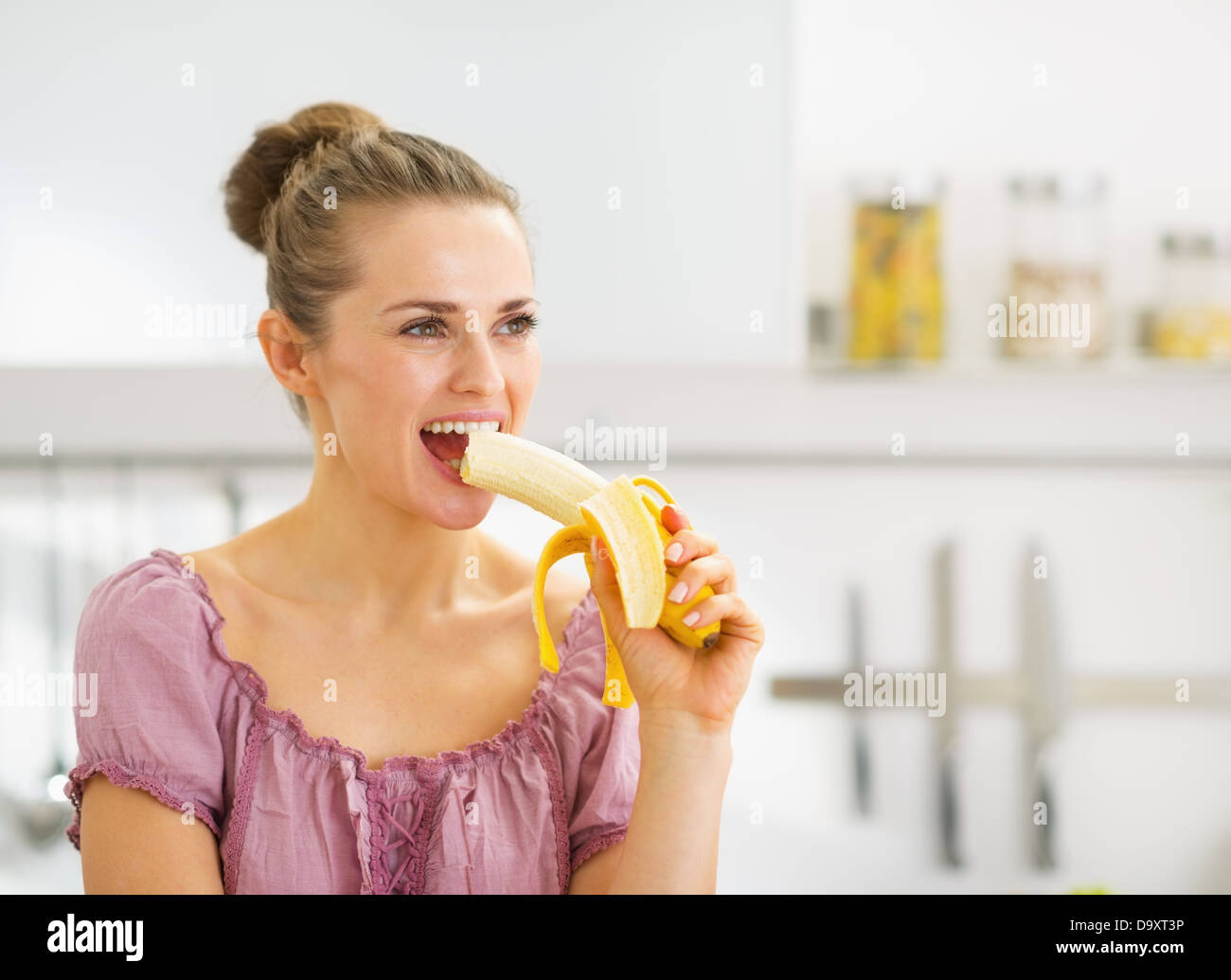 Young woman eating banana in kitchen Stock Photo