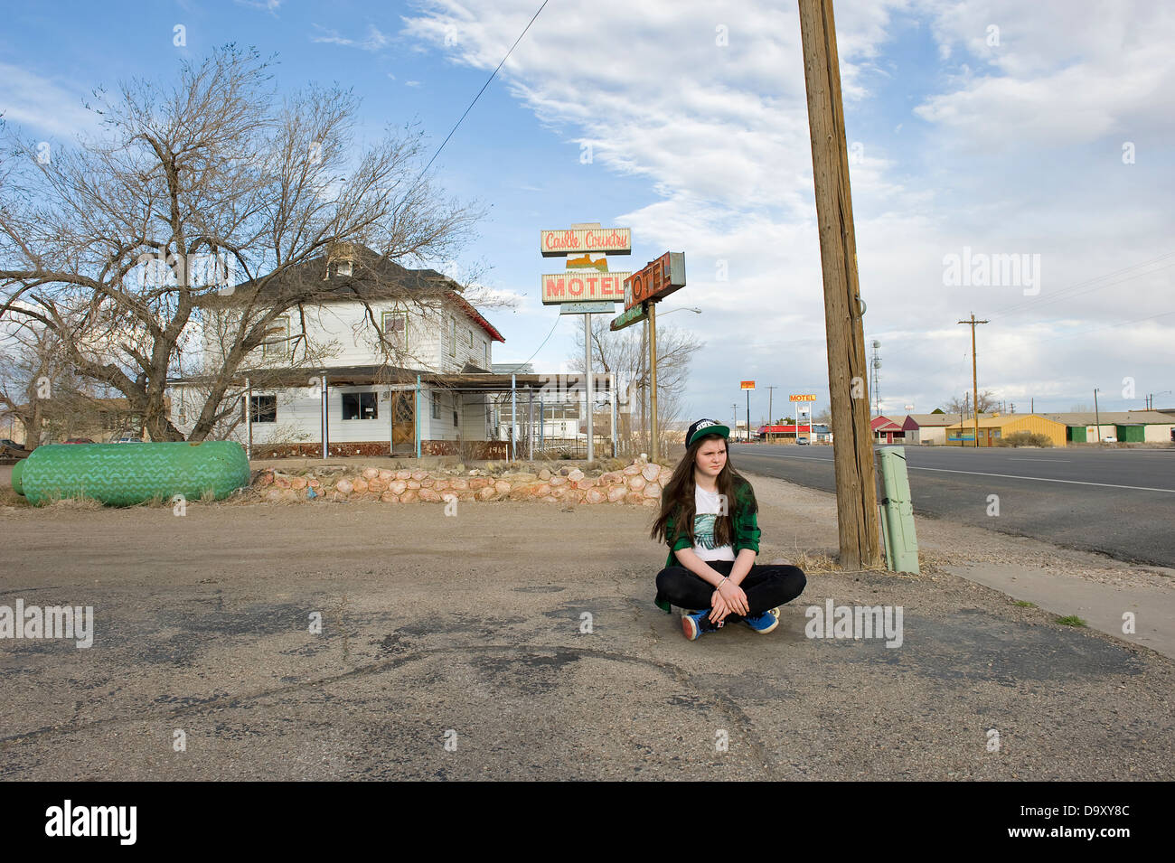 Teenage girl with skateboard sitting outside house wearing Obey cap and green checked shirt, Green River, Utah, USA. Stock Photo
