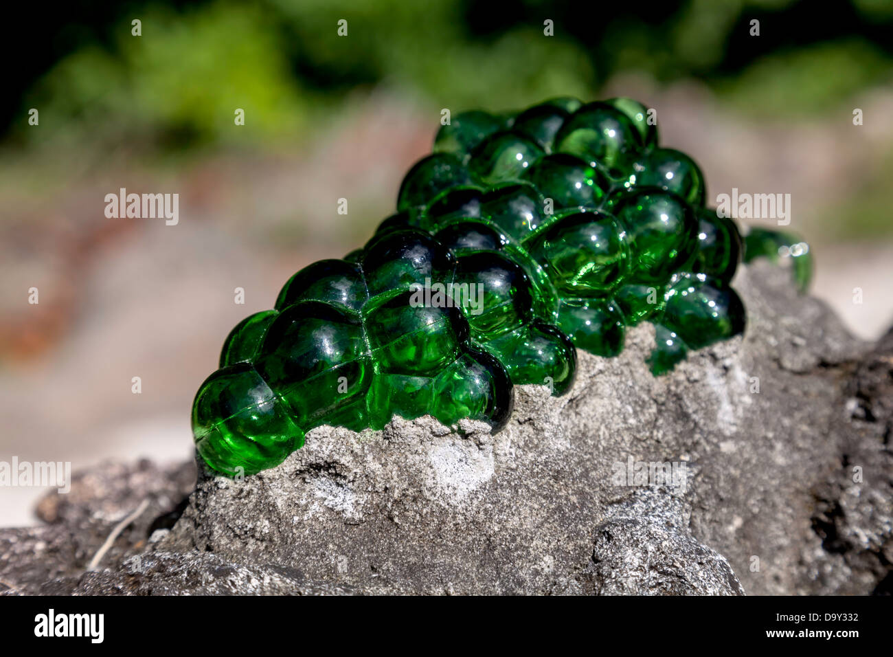 Green glass grapes sculpture embedded on the top of a low stone garden wall. Stock Photo