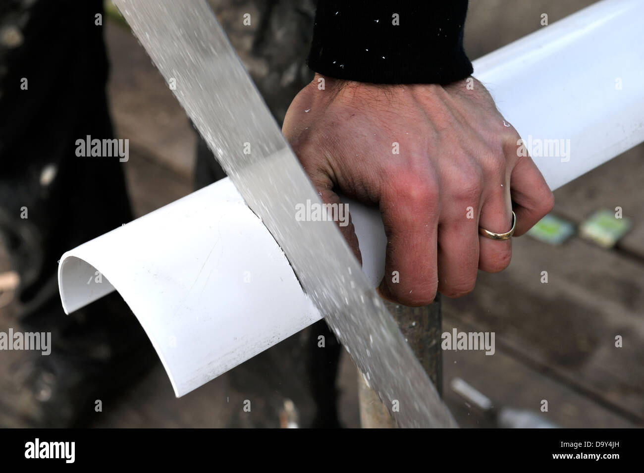 Builder sawing plastic rainwater gutter to length Stock Photo