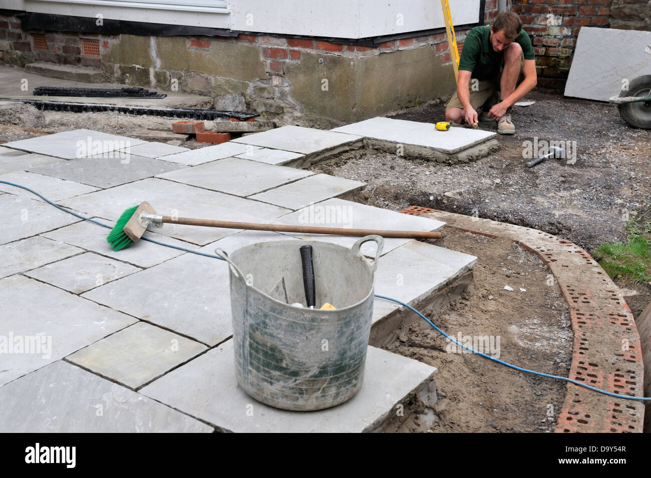 Construction of a patio laying natural stone paving, man adjusting the mortar bed Stock Photo