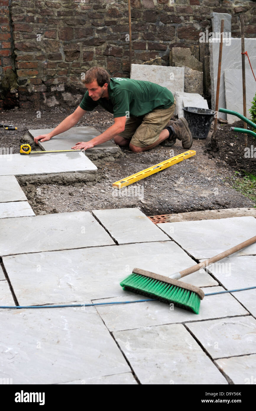 Construction of a patio laying natural stone paving, man measuring position of paving slab Stock Photo