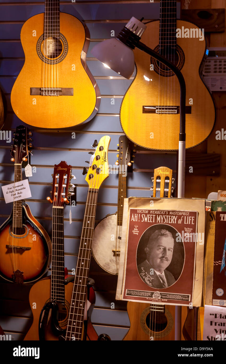 Acoustic guitars, a mandolin and banjo hang on the wall behind sheet music displayed on a music stand. Stock Photo