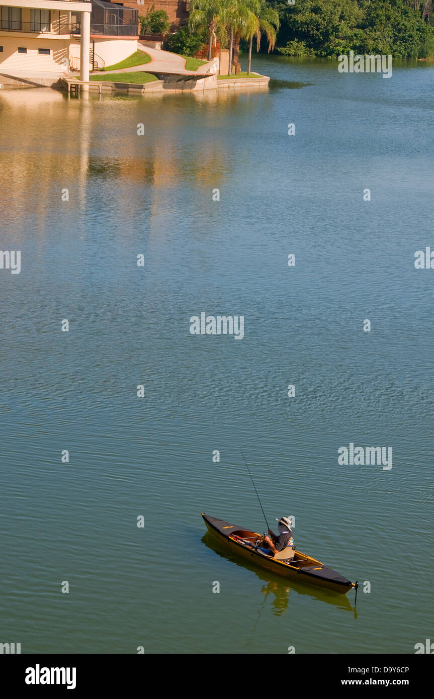 From his canoe, an angler fishes for bass and panfish in a small residential development lake. Stock Photo