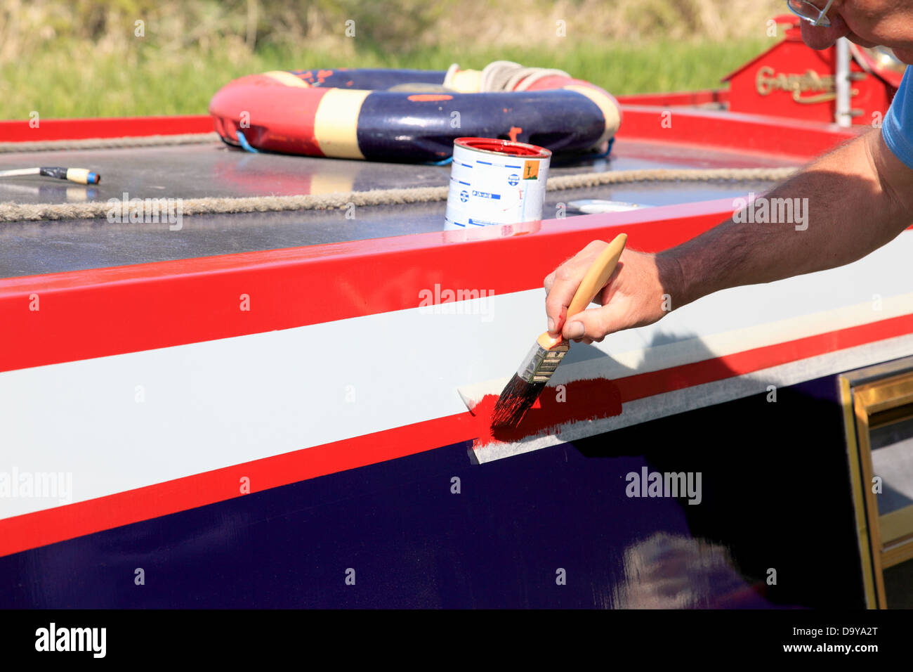 A man using masking tape to paint a red line on the side of his canal