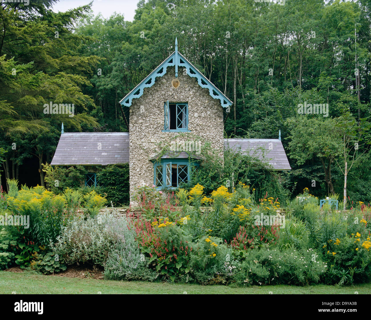 Golden rod growing in borders of stone cottage with pale blue painted barge boarding and windows set in woodland Stock Photo Alamy